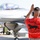 A ground crew member wearing a red 'Panther Pride - GET SOME! Falcon Air Meet 2014' t-shirt is marshaling an F-16 Fighting Falcon fighter jet on a flight line. The aircraft bears the number '411' and a pilot is visible in the cockpit. Several military personnel are standing in the background observing the operation.