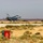 A single-engine fighter jet, identifiable as an F-16 Fighting Falcon, is captured during takeoff or low-altitude flight above a desert airstrip. The aircraft displays a flag marking on its fuselage consistent with the Jordanian flag, suggesting it belongs to the Royal Jordanian Air Force. The surrounding terrain is arid and semi-desert, with sparse scrub vegetation and sandy soil visible in the foreground.