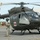 A U.S. Army UH-72 Lakota medical evacuation (MEDEVAC) helicopter is shown on a tarmac or airfield, identifiable by the red cross markings on its fuselage. Several soldiers in Army Combat Uniforms (ACU) are present around the aircraft, with one ground crew member connected via communication cable to the helicopter. The scene appears to be a pre-flight or post-flight ground operation at a military installation.