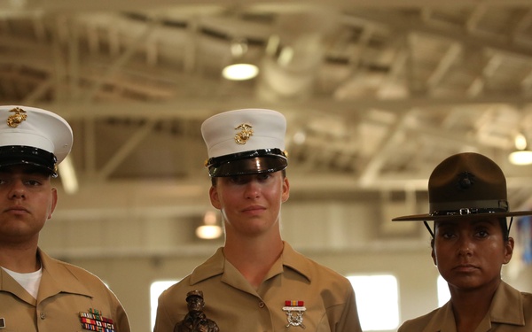 Three U.S. Marine Corps personnel are posed together in a large indoor facility, likely during an awards ceremony. The central figure is holding a trophy bust and a plaque that reads 'Marine Corps Shooting Foundation - High Shooter Award' sponsored by Leupold. The individuals are wearing standard USMC service uniforms with rank insignia and ribbons visible.