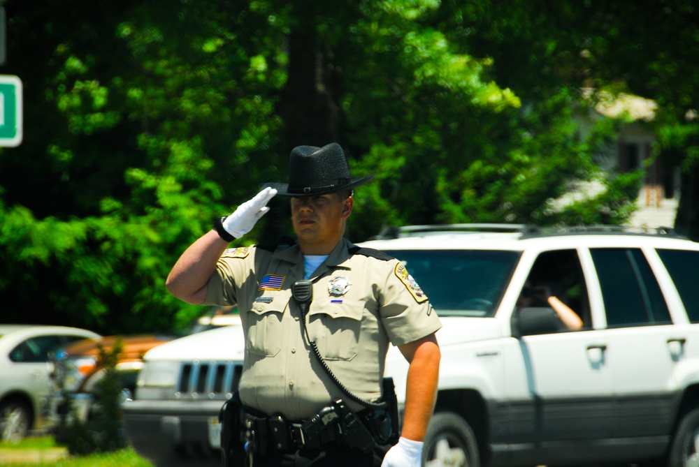 A Stafford County, Virginia, deputy sheriff temporarily closing a roadway, salutes the funeral procession