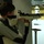 A young person is aiming a precision air rifle at an indoor shooting range. They are wearing a shooting jacket and glove, which are standard competitive shooting equipment. Multiple target stands are visible downrange in the background.