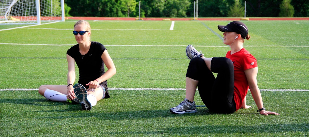 Athletes stretch before competing in the open women's 100 meter at the 2014 Warrior Trials