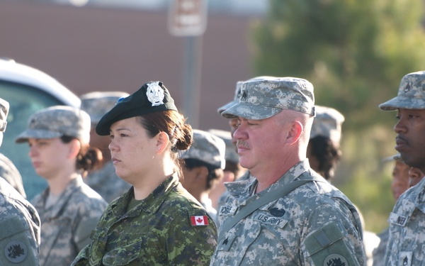 A formation of military personnel standing at attention, featuring both U.S. Army soldiers in ACU (Army Combat Uniform) digital camouflage and one Canadian Armed Forces soldier in CADPAT (Canadian Disruptive Pattern) uniform with a black beret and Canadian flag patch. The group appears to be assembled for a formal military ceremony or parade. The mixed nationality presence suggests a joint military exercise or exchange program.