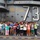A large group of civilian visitors, appearing to be of East Asian origin, pose for a group photo on the flight deck of USS George Washington (CVN-73), a US Navy aircraft carrier. The ship's island superstructure is visible behind them, displaying the hull number '73' and a safety warning reading 'BEWARE OF JET BLAST PROPELLERS AND ROTORS'. The visitors are wearing colorful casual clothing and many are making peace/victory hand signs.