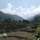 A photograph dated 07/14/2003 showing terraced agricultural hillsides in a mountainous valley region, likely in South or Central Asia based on the terrain and architectural style. Stone-walled terraces step up the hillside with sparse vegetation and what appear to be ruined or damaged stone structures at the top of the terraces. A deep mountain valley recedes into the background under a partly cloudy sky.