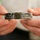 A person is holding a worn and damaged black memorial bracelet (POW/MIA or KIA commemorative wristband). The bracelet bears an inscription honoring a fallen U.S. soldier identified as SFC [M...] KAHLE[R], killed in action on 26 JAN 08 in Afghanistan, associated with Charlie Company, 3rd Airborne Brigade. The bracelet shows significant wear, damage, and debris consistent with long-term use.
