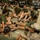 A group of female military recruits in olive green PT (physical training) uniforms are seated on a barracks floor in a circular formation. An instructor in camouflage utilities is present, appearing to conduct a briefing or foot care inspection session. The setting appears to be a military barracks bay with storage lockers visible in the background.