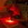 A military service member in camouflage uniform is leaning over a desk, using a red-filtered flashlight to read documents in a darkened environment. The red light illuminates the papers and the soldier's face while preserving night vision. This is a common tactical practice used by military personnel to read maps or documents without compromising night adaptation.