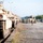 1st Cavalry arrives in Poland A column of desert-tan painted M1 Abrams main battle tanks and Bradley Fighting Vehicles are staged on what appears to be a rail offloading facility or military staging area. Numerous soldiers in camouflage uniforms with high-visibility vests are moving between the vehicles, likely conducting post-transport inspections or marshaling operations. The scene suggests a large-scale military equipment deployment or exercise.