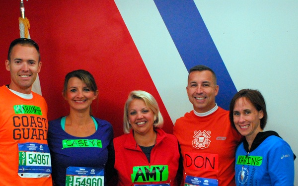 Five runners pose together before a race, wearing numbered bibs sponsored by Tata Consultancy Services (TCS). Two of the runners wear orange shirts with Coast Guard branding, and each runner has their first name displayed on a green label on their bib. The group includes individuals named Casey (54960), Amy (68884), Don (54996), Karine (54994), and an unnamed runner (54967).