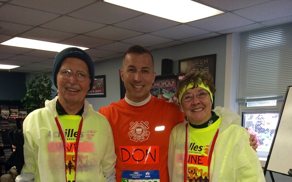Three people pose together indoors, likely before the New York City Marathon. The central figure, identified as 'DON' on his orange shirt, wears race bib number 54996 from the TATA Consultancy Services NYC Marathon. The two flanking individuals wear Achilles International vests with 'GUIDE' bibs, indicating they are volunteer guides for a disabled or visually impaired runner.