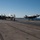 Two F-35C Lightning II stealth fighter jets are visible on the flight deck of a US Navy aircraft carrier. One aircraft appears to be landing or taxiing on the right side of the deck, while another is parked on the left near a jet blast deflector. Several flight deck crew members in colored jerseys are visible attending to operations.