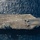 An aerial top-down photograph of a large US Navy aircraft carrier underway in open ocean. The flight deck is largely clear with a small number of aircraft visible on the deck surface. The hull number '68' is visible on the starboard side, identifying this as USS Nimitz (CVN-68).