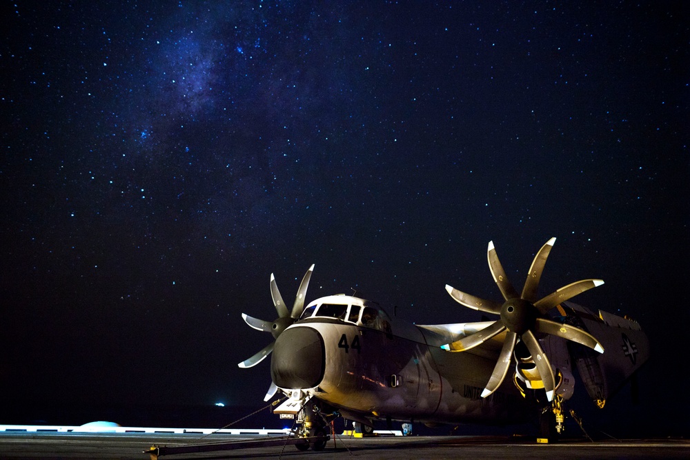 A U.S. Navy C-2A Greyhound aircraft sits on the flight deck of an aircraft carrier underneath a starry sky.