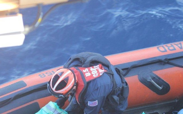 U.S. Coast Guard personnel are conducting an interdiction operation at sea, transferring bundled packages from an inflatable rigid-hull boat (RHIB) to a larger vessel. The orange RHIB is clearly marked 'COAST GUARD' and personnel are wearing standard Coast Guard gear including helmets and life vests. The green-wrapped bundles being handled are consistent with contraband seizure operations.