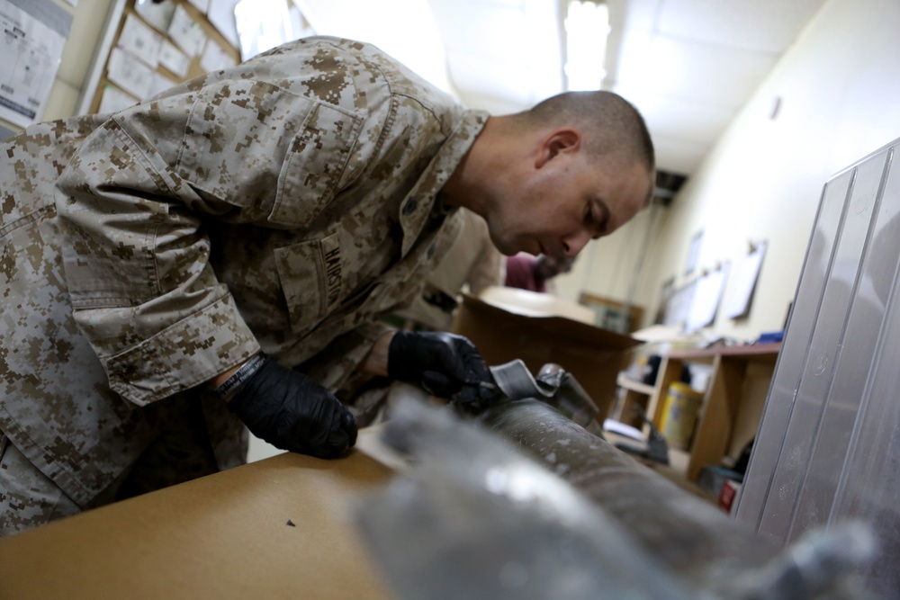 U.S. Marine Gunnery Sgt. Joshua W. Hairston, the Exploitation Analysis Center Lab Chief Special Purpose Marine Air Ground Task Force – Crisis Response – Central Command scrapes paint off exploded ordnance on Dec. 30, 2014.
