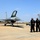 A military flight line scene showing at least two F-16 Fighting Falcon jets marked with 'WW' tail codes, indicating assignment to Misawa Air Base, Japan. Four personnel — three in black uniforms and one in a flight suit — stand on the tarmac observing the aircraft. The canopy of the foreground F-16 is open, suggesting pre-flight or post-flight operations.