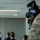 2015 Australian International Airshow and Aerospace & Defence Exposition A military press conference or briefing is being filmed by a Canon professional video camera. A uniformed military officer stands at a podium addressing an audience, while attendees in both civilian and military attire observe. The camera's LCD screen displays a live feed of the speaker at the podium.