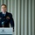 2015 Australian International Airshow and Aerospace & Defence Exposition A military officer in a dark navy dress uniform is speaking at a podium during a formal event at Crown Events & Conferences. He is wearing pilot wings, service ribbons, and gold buttons, indicating a senior rank in an air force. A second person is partially visible in the foreground, seated with their back to the camera.