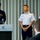 2015 Australian International Airshow and Aerospace & Defence Exposition Three military officers are standing at a press conference or official briefing held at a Crown Events & Conferences venue. One officer in a dark navy uniform stands at the podium with microphones, while two others in light blue uniforms stand behind him. A civilian figure is visible in the foreground with their back to the camera.