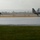 2015 Australian International Airshow and Aerospace & Defence Exposition Two stealth fighter jets, identifiable as F-22 Raptors, are taxiing on a wet runway during rainy conditions. The tarmac is heavily flooded with standing water, and a red and yellow safety barrier fence runs along the runway edge. The overcast weather and rain significantly reduce visibility in the background.