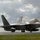 2015 Australian International Airshow and Aerospace & Defence Exposition A U.S. Air Force F-22 Raptor stealth fighter jet is taxiing on a wet runway, likely following recent rainfall. The aircraft displays tail code 'HH' indicating assignment to Hickam Air Force Base, Hawaii. The low-angle shot captures the aircraft's distinctive stealth geometry against a dramatic cloudy sky.
