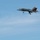 2015 Australian International Airshow and Aerospace & Defence Exposition A military jet fighter is captured in flight against a clear blue sky with light cirrus clouds. The aircraft has its landing gear fully extended, suggesting it is on approach for landing. The tail section features a distinctive red and white livery consistent with Royal Australian Air Force (RAAF) markings.