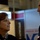 2015 Australian International Airshow and Aerospace & Defence Exposition Two individuals in dark uniforms are engaged in a face-to-face conversation at what appears to be a trade show, conference, or exhibition environment. The woman on the left is looking up attentively at the man on the right, who appears to be speaking. Both wear lanyards and insignia consistent with military or official service uniforms.