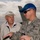 2015 Australian International Airshow and Aerospace & Defence Exposition Two men are conversing on an airfield tarmac at what appears to be the Australian International Airshow. One man is an older civilian wearing a 'Sun Valley' jacket and a white cap, while the other is a younger US Air Force servicemember in ABU (Airman Battle Uniform) with a 'PARTICIPANT' cap and a lanyard reading 'Australian International Airshow'. An aircraft tail fin is visible in the background.