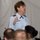 2015 Australian International Airshow and Aerospace & Defence Exposition A female military officer in a light blue Air Force dress uniform is addressing an audience. She appears to be speaking at a formal briefing or presentation, holding what appears to be a note card. Several audience members are visible in the foreground, slightly out of focus.