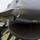2015 Australian International Airshow and Aerospace & Defence Exposition A military pilot or crew member in an olive green flight suit is conducting a pre-flight or post-flight inspection of a fighter jet, likely an F-16 Fighting Falcon. The individual is examining the underside of the aircraft near the engine intake area. The image is taken from a close, low angle emphasizing the aircraft's fuselage and intake.