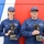 2014 Coast Guard Sector Buffalo EPOY and REPOY award Two U.S. Coast Guard personnel in blue uniforms are posing with trophy awards in front of a red, white, and blue painted wall. Their name tapes read 'GAULT' (female, left) and 'ALLING' (male, right), and both are holding identical bronze bison head trophies on black bases. The plaques on the trophies appear to indicate 'Volunteer Person of the Year' awards.