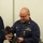 Coast Guard Sector Buffalo 2014 EPOY award A U.S. Coast Guard petty officer named Alling is holding and examining a bronze animal figurine trophy or award mounted on a dark base. He is wearing a navy blue Coast Guard uniform with visible rank insignia, a name tape, branch tape, a qualification badge, and a medal with a green and orange ribbon. The setting appears to be an indoor facility, likely during an awards or recognition ceremony.
