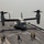 Osprey makes first ever landing on Republic of Korea amphibious assault ship A U.S. Marine Corps MV-22 Osprey tiltrotor aircraft is on the flight deck of a naval vessel, with its rotors spinning in helicopter mode. Several deck crew members in colored vests and helmets are visible on the flight deck, appearing to conduct flight operations. The vessel is at sea, with open water visible in the background.