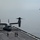 Osprey makes first ever landing on Republic of Korea amphibious assault ship A Bell Boeing V-22 Osprey tiltrotor aircraft sits on the flight deck of a naval vessel with its rotors spinning, suggesting it is preparing for takeoff or has just landed. Three flight deck crew members in colored safety vests are visible on the deck near the aircraft. A second large naval vessel, likely an amphibious assault ship or aircraft carrier, is visible in the background on the water.