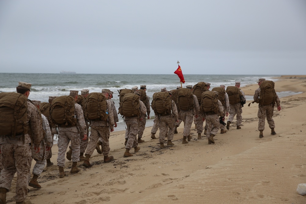 Marines and sailors hike on the beach