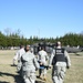 Military personnel in U.S. Army ACU (Army Combat Uniform) are carrying a patient on a stretcher toward a UH-60 Black Hawk helicopter for a medical evacuation (MEDEVAC). One individual is wearing a black tactical vest labeled 'CST MEDICAL' and communications headset. This appears to be a training exercise or real casualty evacuation scenario on an open grassy field.