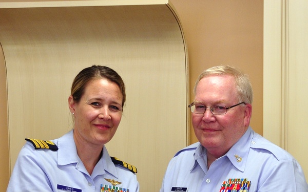 Two United States Coast Guard personnel in light blue uniforms are jointly holding a framed Certificate of Retirement. The certificate is being presented to Senior Chief Yeoman Richard P. Maher from the United States Coast Guard Reserve. Both individuals are displaying multiple service ribbons and medals on their uniforms.