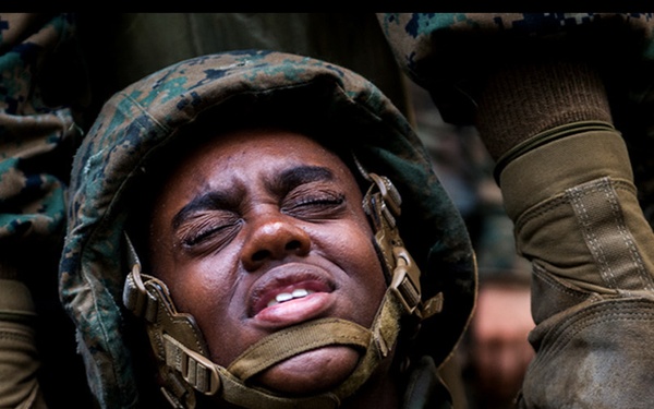 A photo collage depicting what appears to be military training or boot camp activities, likely U.S. Marine Corps based on the camouflage uniforms and gear visible. The central and dominant image shows a recruit in distress or intense physical exertion wearing a combat helmet and camouflage uniform. The surrounding panels capture various stages of training including group formations, field exercises, and nighttime drills.
