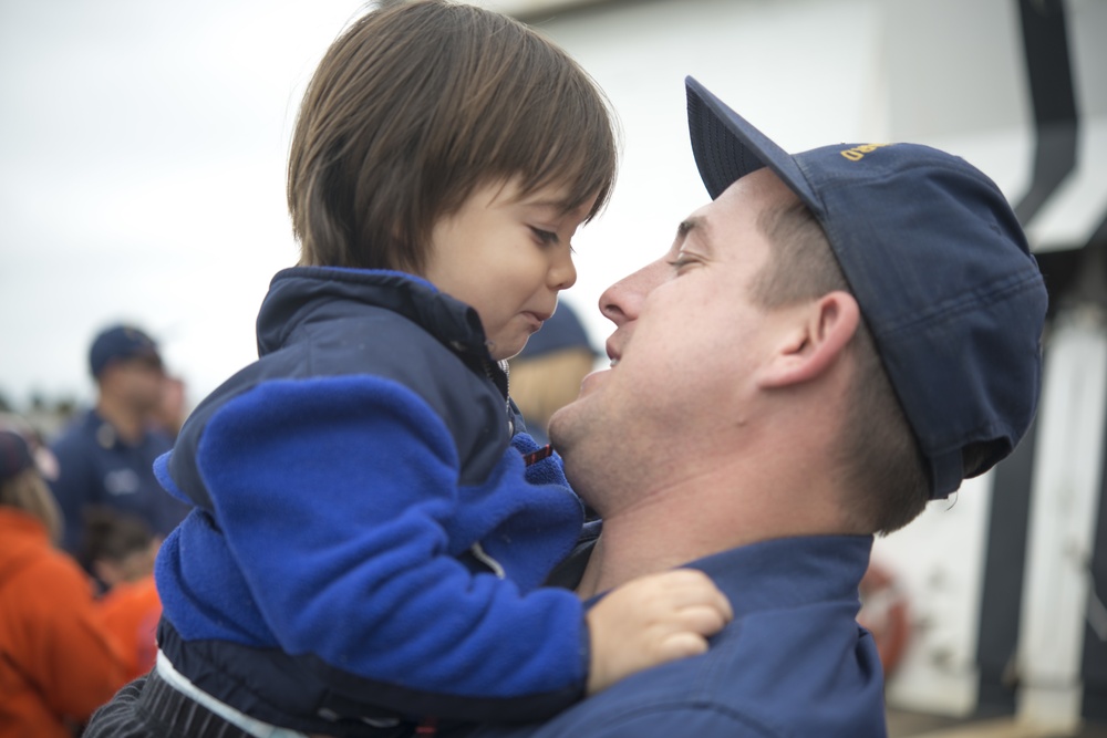 A US Coast Guard Bertholf crew member embraces his son after returning to homeport