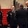 A formal U.S. Army military ceremony is taking place in what appears to be a large indoor venue with red-carpeted steps in the background. Four soldiers in Army Service Uniform (dress blues) are engaged in conversation, with one soldier facing away from the camera appearing to interact with the central figure. The central soldier's name tape reads 'MOETZELMANN' and displays Sergeant Major rank insignia.