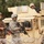 The image shows military personnel from what appears to be a joint operation, with at least one U.S. Army soldier identifiable by the American flag patch and ACU (Army Combat Uniform) pattern. They are positioned near a tan/desert-colored armored military vehicle, likely an MRAP or up-armored HMMWV, with razor wire visible in the foreground. A third soldier is visible in the vehicle's gun turret position.