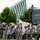 2015 Department of Defense Warrior Games Opening Ceremony A group of individuals in matching gray athletic uniforms are participating in what appears to be a formal parade or ceremonial procession. The group includes both ambulatory participants and individuals using wheelchairs, suggesting this is likely a military or veterans' athletic event such as the Warrior Games or Invictus Games. An American flag is being carried at the front of the procession, and a large LED display screen is visible in the background.