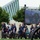 2015 Department of Defense Warrior Games Opening Ceremony A group of individuals wearing matching navy blue and white athletic uniforms, some in wheelchairs, are gathered at an outdoor event. The word 'NAVY' is visible on several uniforms, suggesting this is a military-affiliated athletic event, possibly the Warrior Games or a similar adaptive sports competition. A large LED display screen mounted on a truss structure is visible in the background, along with a modern building and trees.