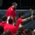 2015 Department of Defense Warrior Games Opening Ceremony A group of individuals wearing matching red polo shirts are gathered at what appears to be a ceremonial event. One person with a tattooed arm is prominently holding a lit torch aloft, suggesting an opening or closing ceremony. The setting appears to be an indoor arena or stadium.
