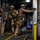 Maritime Raid Force, 26th MEU conducts VBSS training Three armed military or law enforcement personnel in full tactical gear are conducting what appears to be a ship boarding or vessel clearance operation. They are positioned at a doorway/hatch on what appears to be a large vessel, with one operator pointing a rifle through the opening. The setting is an industrial interior space consistent with a cargo ship or naval vessel.