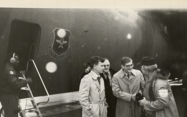 Two men and woman in front of aircraft carrier