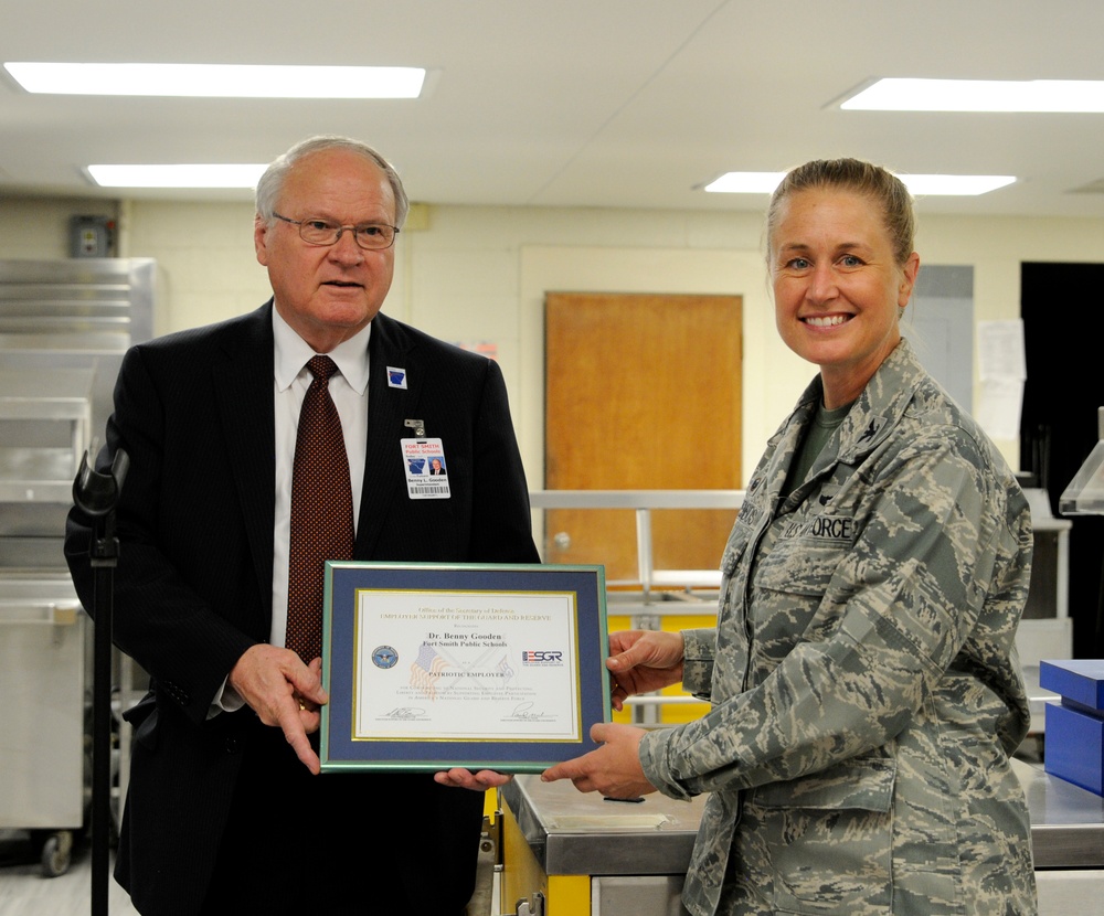 A civilian man and a U.S. Air Force service member are jointly holding a framed certificate in what appears to be an institutional or school cafeteria setting. The certificate is from the ESGR (Employer Support of the Guard and Reserve), issued under the Office of the Secretary of Defense, recognizing 'Dr. Benny Gooden' of 'Fort Smith Public Schools' as a 'Patriotic Employer.' This appears to be a formal award presentation ceremony.
