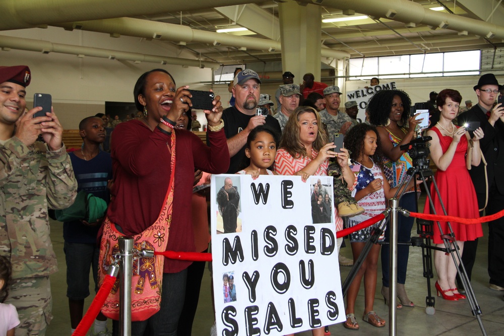 Family and friends of the returning Soldiers of Blue Team, 1st Sustainment Command (Theater) cheer and display signs at Pope Army Airfield, Aug. 24 as they return from a nine-month deployment to Kuwait